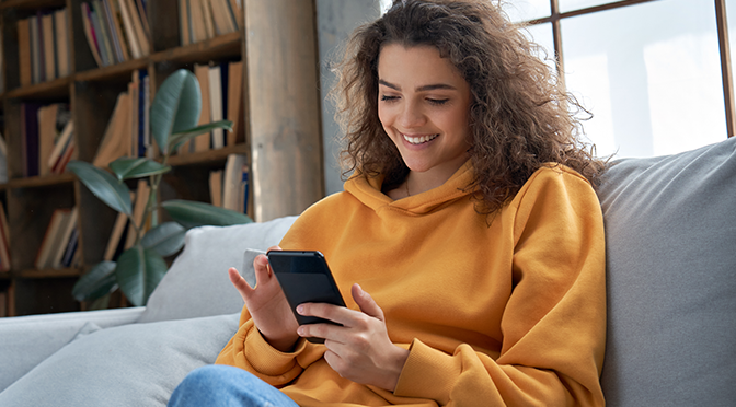 Happy millenial hispanic Mädchen überprüfen Social Media, hält Smartphone zu Hause. Lächelnd junge Latina mit Handy App spielen Spiel, online einkaufen, die Lieferung bestellen entspannen auf Sofa.