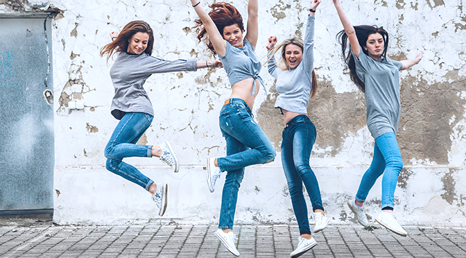 Gruppe von vier jungen Mädchen mit grauem T-Shirt und Jeans, die auf einer groben Straßenwand stehen, Mode-urbane Kleidung-Stil, signature look