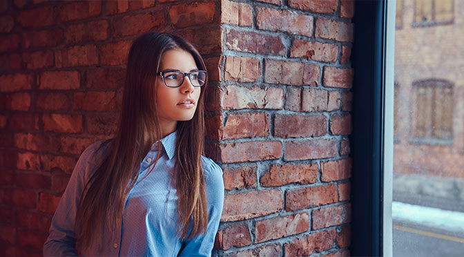 portrait attractive charming brunette glasses blue shirt leaning against brick wall room with loft design