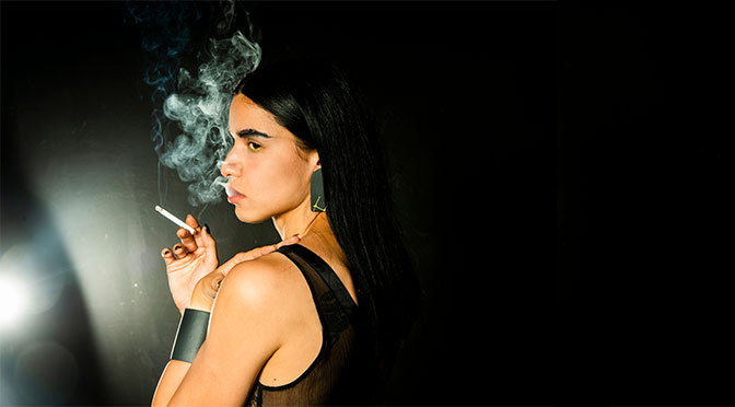 Mysteriöse junge Frau in Schwarz, umgeben von Rauch aus ihrer Zigarette
