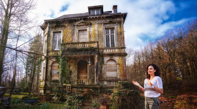 junge Frau steht vor einer alten, verlassenen Villa
