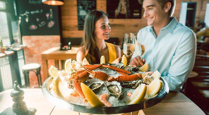 Nahaufnahme frischer Austern und Krabben, die auf Eis serviert werden, mit Zitronenscheiben am Tisch eines romantischen jungen Paares, das im Restaurant isst