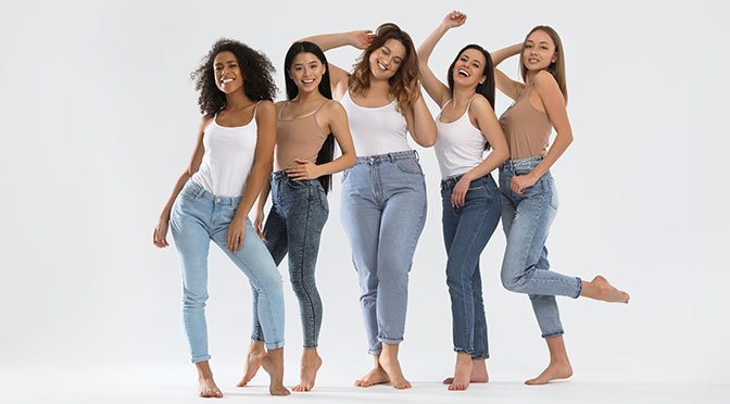 Group of women with different body types on light background, wearing jeans while being barefoot