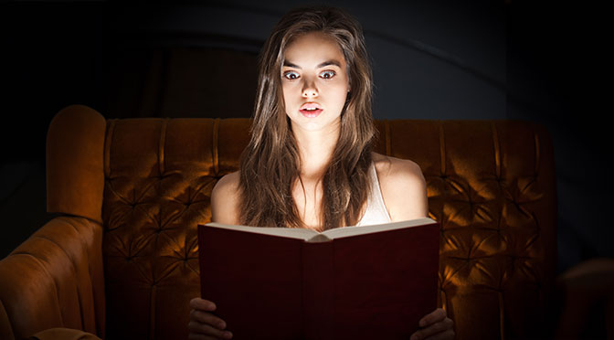 Schöne schockierte junge brunette Frau liest Buch in kreativer Beleuchtung.