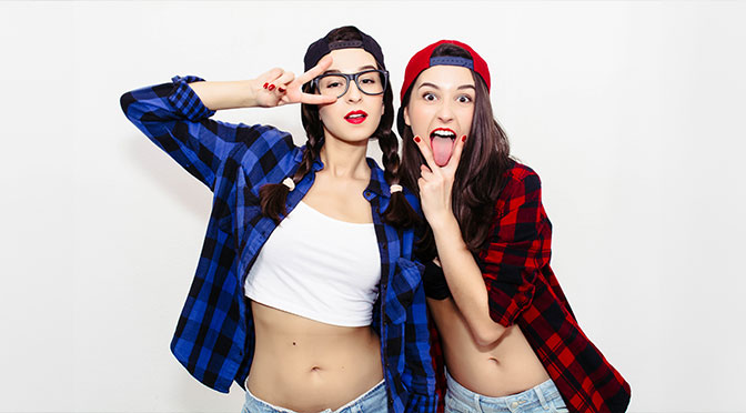 Spaß Mädchen halten Zunge heraus zwischen zwei Fingern zeigen cunnilingus Schild. Farbige Comic lustige emotionale hipster Sommer Stil Zwillinge Teenager Mädchen machen Gesichter und Spaß. Einzeln auf grauem Hintergrund.