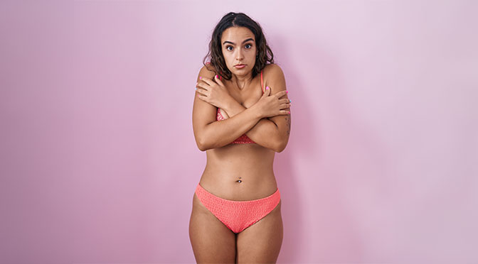 Young hispanic woman wearing lingerie over pink background shaking and freezing for winter cold with sad and shock