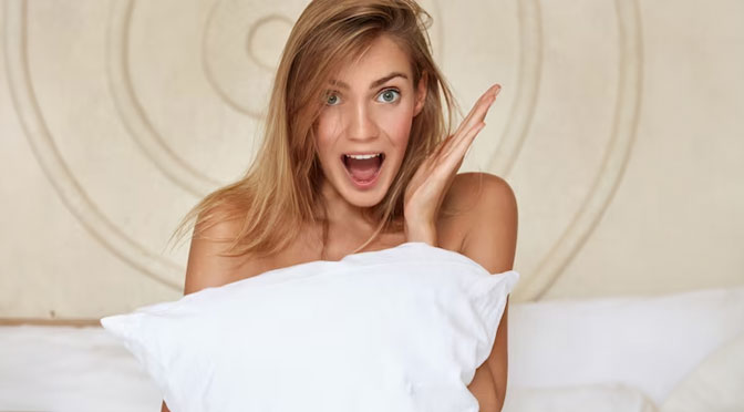 Pretty woman in bed covering herself with pillow