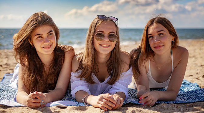 Drei Frauen, 19 Jahre alt, liegen am Strand auf einer Decke und sonnenbaden.