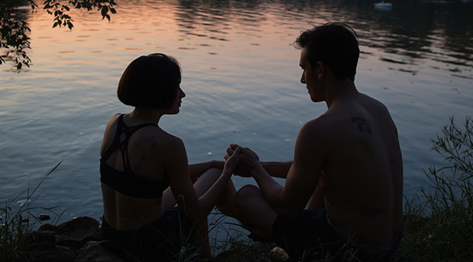 Ein ruhiges Seeufer bei Dämmerung. Wasser plätschert sanft ans Ufer. Blätter rascheln im Wind. Mia, eine junge Frau mit kurzem Haar, sitzt dort. Sie ist zierlich und athletisch. Narben an ihren Armen erzählen von Missbrauch. Psychologisch ist sie misstrauisch. Doch sie sucht Verbindung. Alex, ein sensibler Mann, setzt sich zu ihr. Sein Körper ist schlank und definiert. Er berührt ihre Hand.