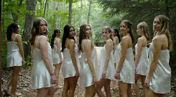 Gruppe junger Sorority-Schwestern, ca. 19 Jahre alt, auf einem schmalen Waldweg, bekleidet nur mit dünnen, weißen Nachthemden, die ihnen bis an die Oberschenkel reichen. barfuß.